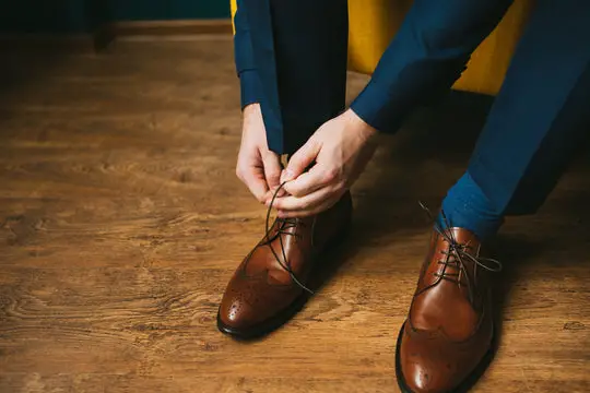 Man tying brown dress shoes wearing suit